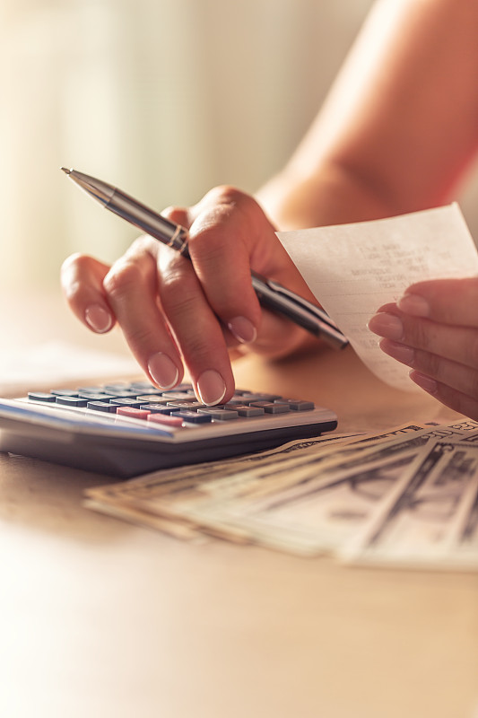 女性手中拿着一张旁边有美元纸币的钞票,手里拿着计算器的细节。图片下载